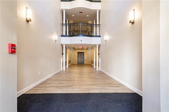 hall featuring decorative columns, a towering ceiling, baseboards, and wood finished floors