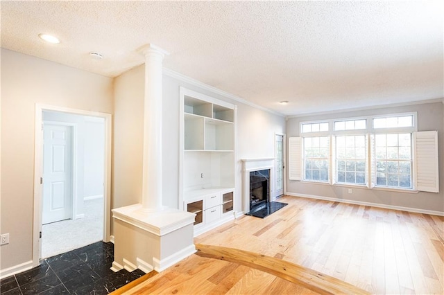 unfurnished living room with a textured ceiling, dark wood-style flooring, a high end fireplace, baseboards, and decorative columns