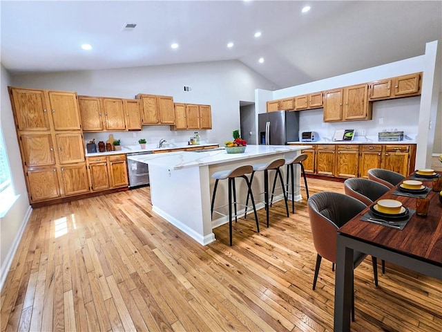 kitchen with a breakfast bar area, high vaulted ceiling, stainless steel appliances, light hardwood / wood-style floors, and a kitchen island