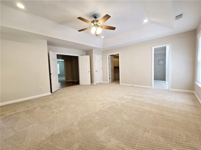 carpeted spare room with a raised ceiling and ceiling fan