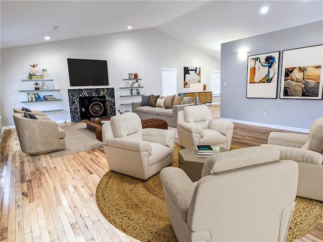 living room with a high end fireplace, vaulted ceiling, and light wood-type flooring