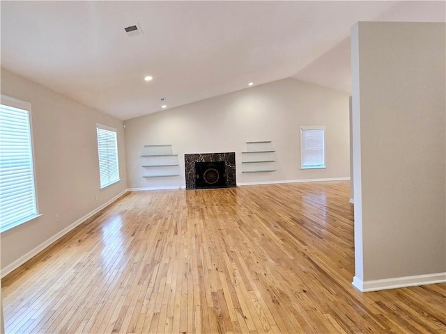 unfurnished living room featuring a premium fireplace, lofted ceiling, light wood-type flooring, and built in shelves