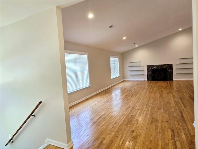 unfurnished living room featuring a premium fireplace, vaulted ceiling, and light hardwood / wood-style floors