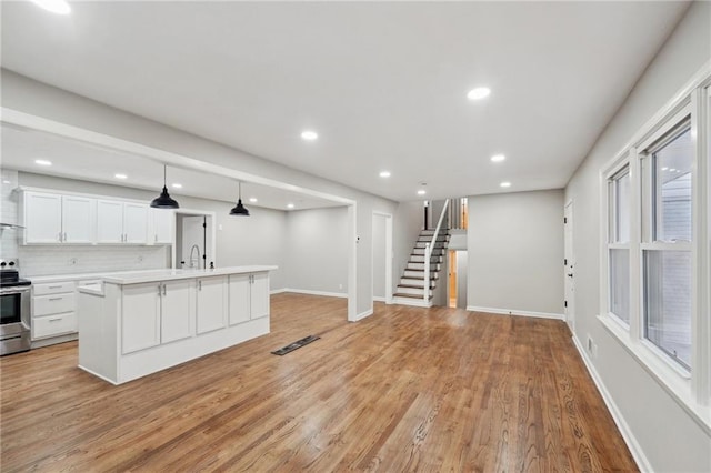 kitchen with backsplash, a kitchen island with sink, sink, light hardwood / wood-style flooring, and white cabinetry