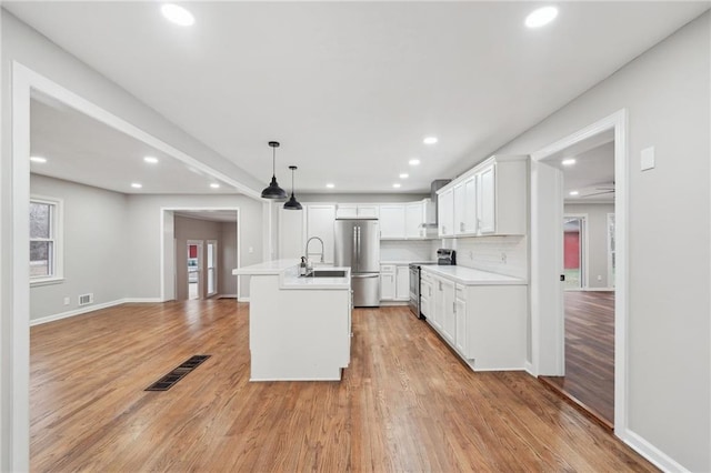 kitchen with a kitchen island with sink, hanging light fixtures, stainless steel appliances, decorative backsplash, and white cabinets