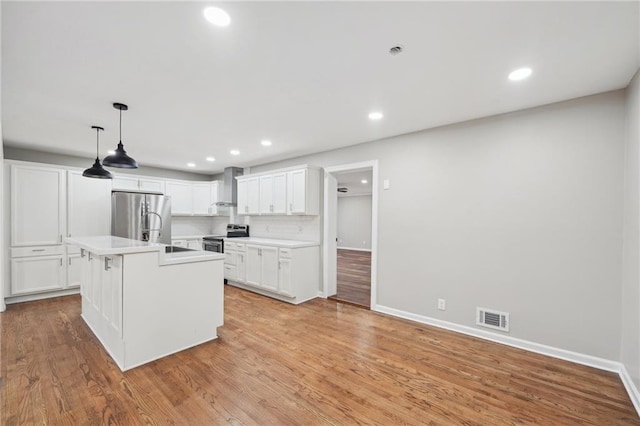 kitchen with decorative backsplash, appliances with stainless steel finishes, wall chimney exhaust hood, a center island with sink, and white cabinets