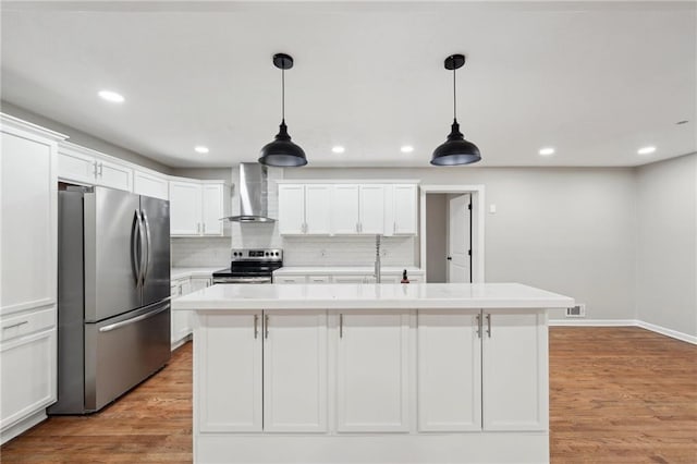 kitchen with white cabinetry, wall chimney exhaust hood, stainless steel appliances, pendant lighting, and a kitchen island with sink