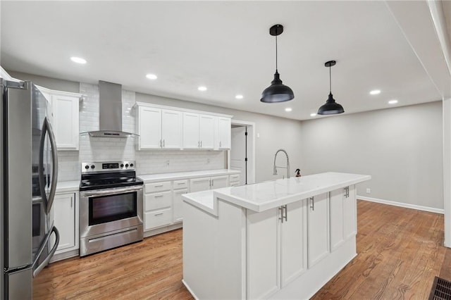 kitchen with decorative backsplash, stainless steel appliances, wall chimney range hood, decorative light fixtures, and white cabinets