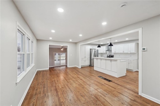 kitchen featuring ceiling fan, an island with sink, decorative light fixtures, white cabinetry, and stainless steel refrigerator