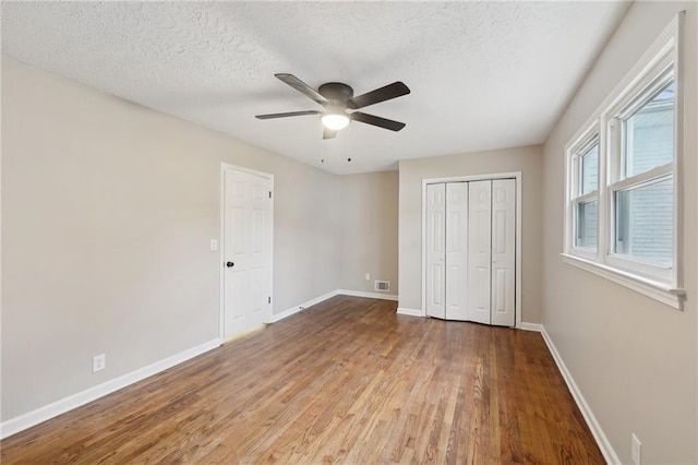 unfurnished bedroom featuring ceiling fan, a closet, a textured ceiling, and light wood-type flooring