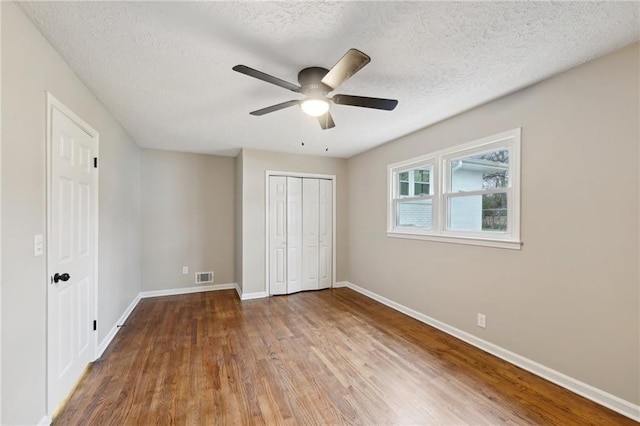 unfurnished bedroom with ceiling fan, a closet, wood-type flooring, and a textured ceiling