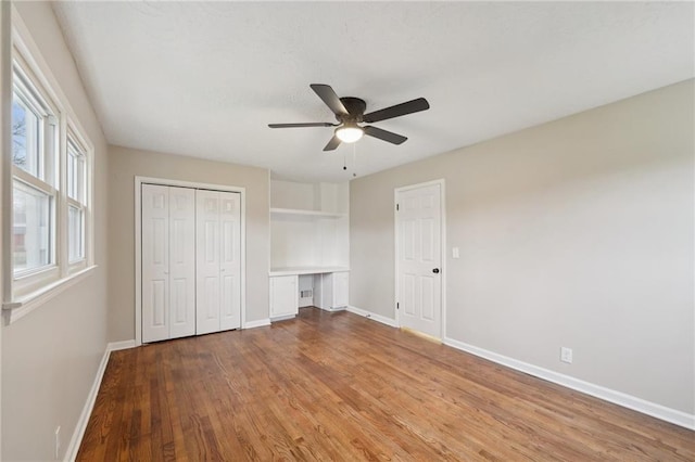 unfurnished bedroom with ceiling fan, built in desk, and light hardwood / wood-style floors