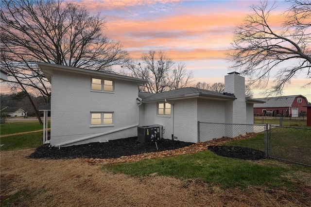 back house at dusk with a lawn and central air condition unit