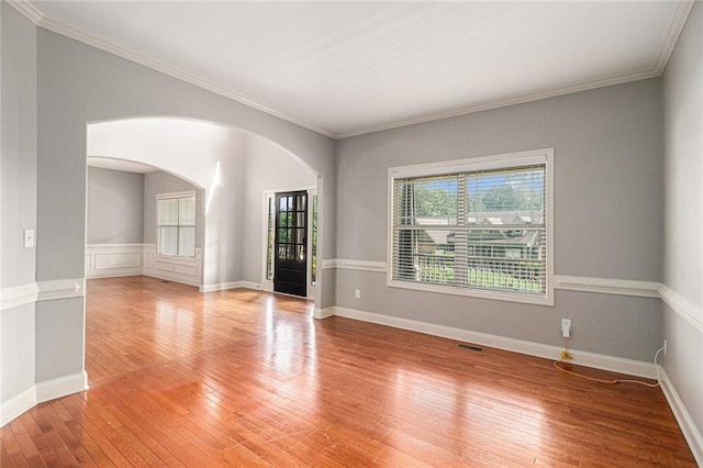 unfurnished room with arched walkways, light wood-style flooring, ornamental molding, and baseboards