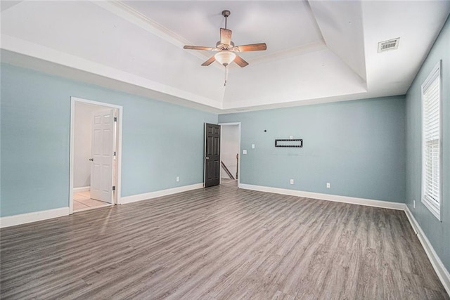 spare room with a tray ceiling, ceiling fan, wood finished floors, and baseboards