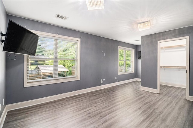 unfurnished bedroom with wood finished floors, baseboards, a closet, and a spacious closet