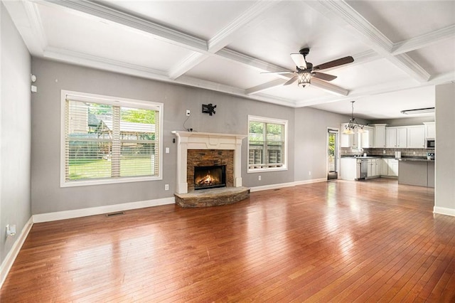 unfurnished living room with hardwood / wood-style flooring, baseboards, coffered ceiling, a stone fireplace, and beam ceiling