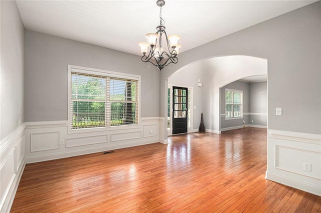 spare room with arched walkways, a chandelier, a wainscoted wall, and light wood-style floors