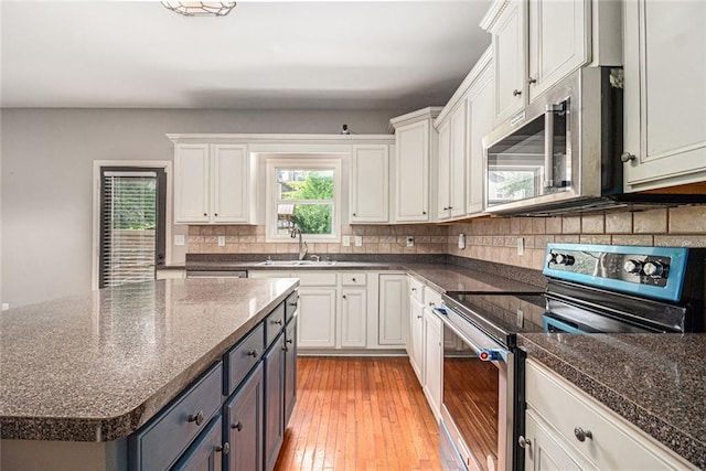 kitchen with stainless steel appliances, backsplash, white cabinets, light wood-type flooring, and a sink
