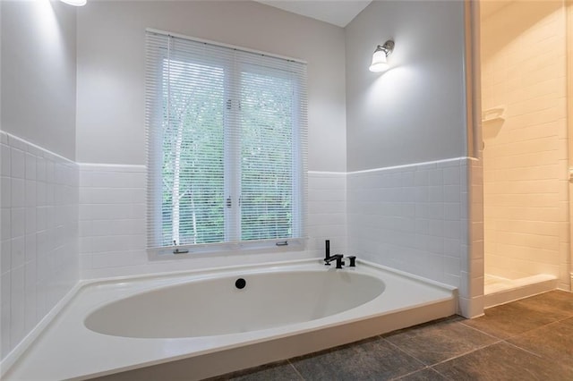 bathroom with a bath, a wainscoted wall, tiled shower, and tile patterned floors