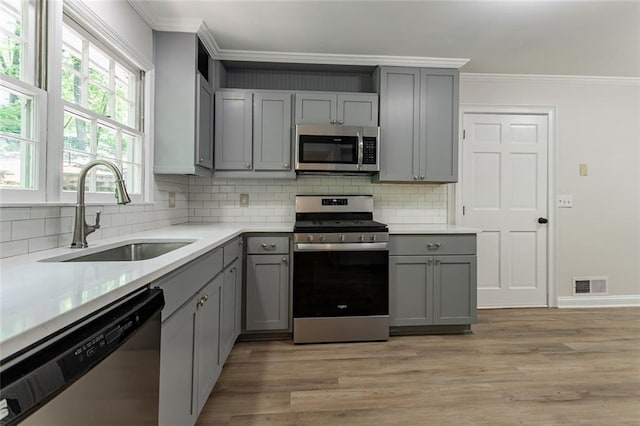 kitchen with crown molding, gray cabinetry, a sink, and stainless steel appliances
