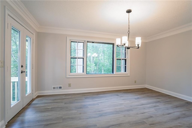 spare room featuring a notable chandelier, a healthy amount of sunlight, wood finished floors, and crown molding