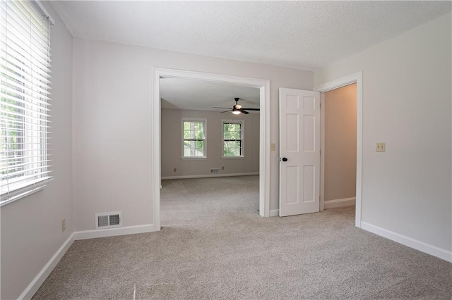 carpeted empty room featuring a textured ceiling, visible vents, ceiling fan, and baseboards