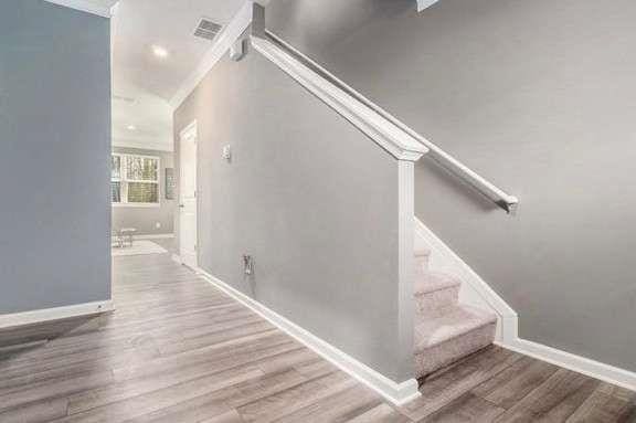 stairs featuring visible vents, crown molding, baseboards, and wood finished floors