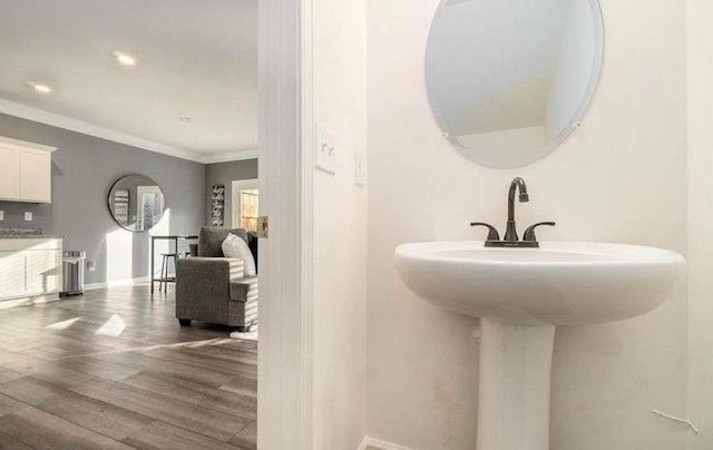 bathroom featuring recessed lighting, ornamental molding, a sink, wood finished floors, and baseboards