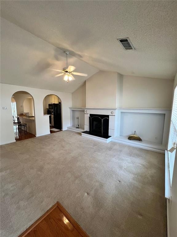 unfurnished living room featuring ceiling fan, carpet flooring, vaulted ceiling, and a textured ceiling