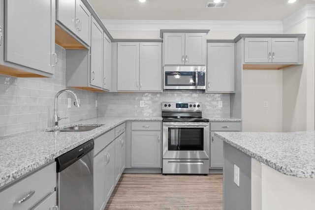 kitchen with light wood-style flooring, ornamental molding, gray cabinets, a sink, and appliances with stainless steel finishes