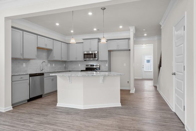 kitchen featuring crown molding, decorative backsplash, gray cabinets, wood finished floors, and stainless steel appliances