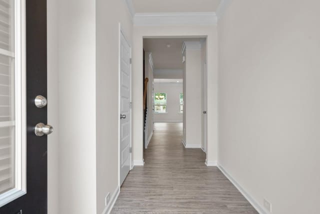 corridor featuring baseboards, light wood-style floors, and ornamental molding