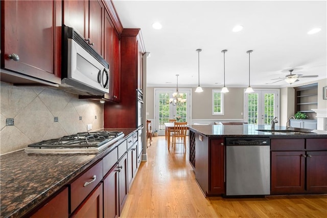 kitchen with appliances with stainless steel finishes, dark stone counters, ceiling fan with notable chandelier, decorative light fixtures, and light hardwood / wood-style floors