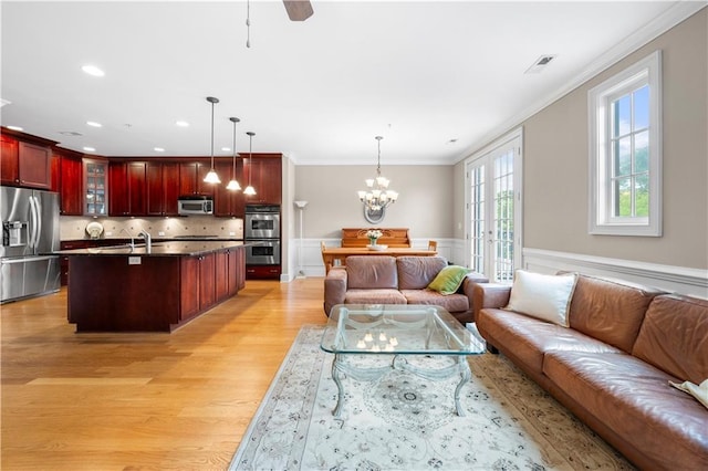 living room featuring french doors, light wood-type flooring, crown molding, sink, and a notable chandelier