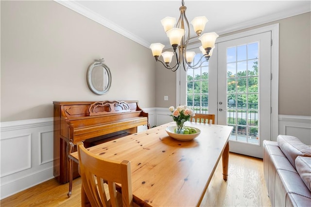 dining area featuring french doors, light wood-type flooring, ornamental molding, and an inviting chandelier