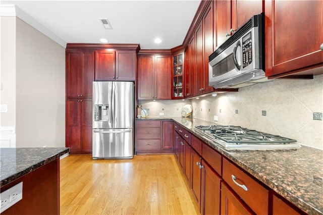 kitchen featuring backsplash, dark stone counters, light wood-type flooring, appliances with stainless steel finishes, and ornamental molding