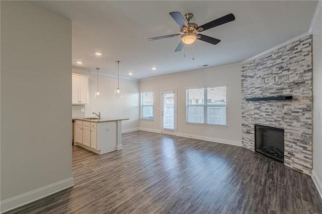 unfurnished living room featuring dark hardwood / wood-style floors, a fireplace, sink, ornamental molding, and ceiling fan