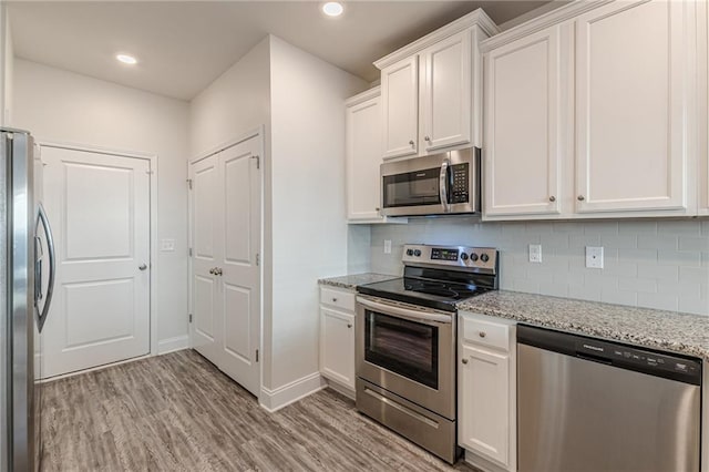 kitchen with appliances with stainless steel finishes, backsplash, white cabinets, light stone counters, and light wood-type flooring