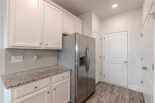 kitchen with stainless steel fridge, white cabinets, light stone countertops, light hardwood / wood-style floors, and backsplash