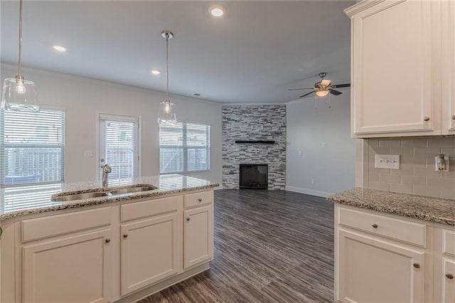 kitchen featuring a stone fireplace, sink, hanging light fixtures, and white cabinets