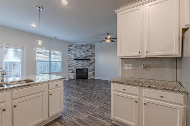 kitchen featuring sink, a stone fireplace, white cabinetry, decorative backsplash, and decorative light fixtures