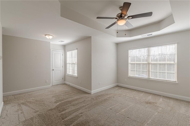 unfurnished room with ceiling fan, a tray ceiling, and light carpet