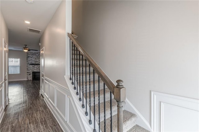 stairs featuring ceiling fan, wood-type flooring, and a stone fireplace