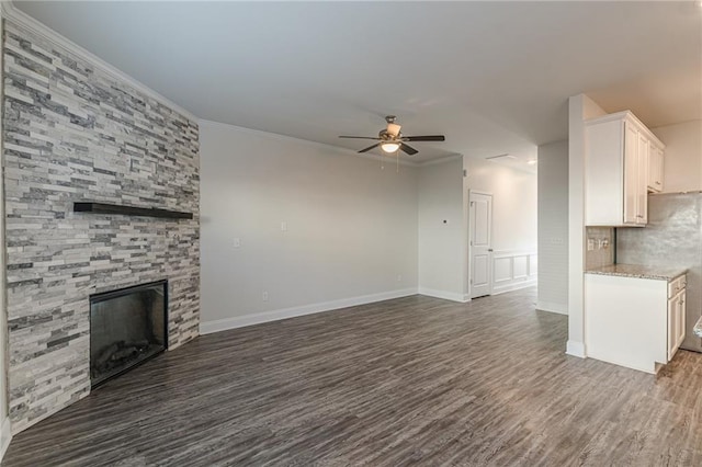 unfurnished living room with a stone fireplace, dark wood-type flooring, ornamental molding, and ceiling fan