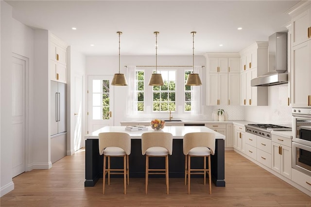 kitchen with hanging light fixtures, stainless steel gas cooktop, wall chimney exhaust hood, a center island, and light hardwood / wood-style floors