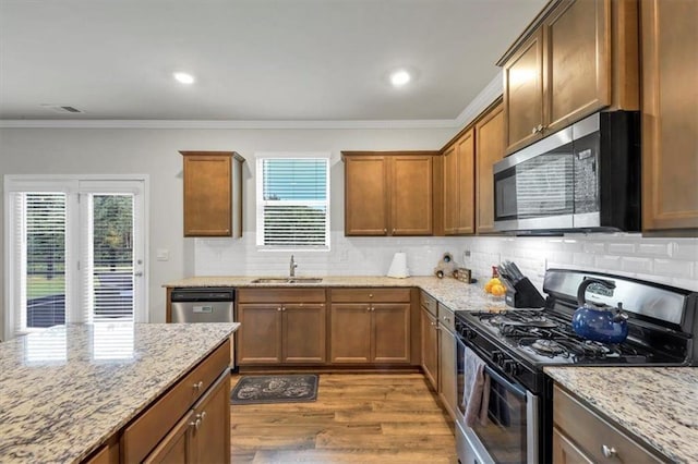 kitchen with sink, decorative backsplash, light stone counters, stainless steel appliances, and light hardwood / wood-style flooring