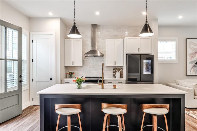 kitchen featuring a healthy amount of sunlight, wall chimney range hood, refrigerator with glass door, and decorative backsplash