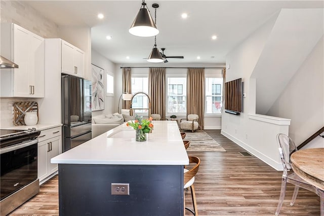 kitchen featuring appliances with stainless steel finishes, open floor plan, wood finished floors, white cabinetry, and a sink