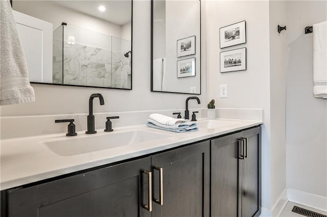 bathroom with double vanity, tiled shower, a sink, and visible vents